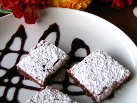 Potete spolverare i tocchetti di torta al cioccolato e mandorle con dello zucchero al velo e decorare il piatto con del cioccolato fuso o a scaglie.